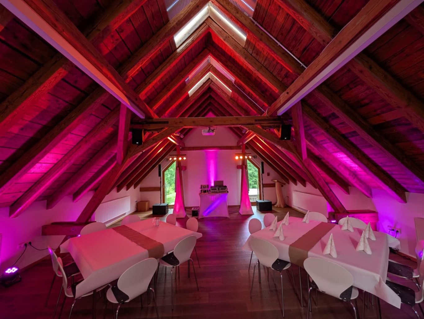 Hochzeitsfeier im Forsthaus Hohenroth Großer Raum mit hohen, holzvertäfelten Wänden und pinker Beleuchtung, gedeckte Tische.