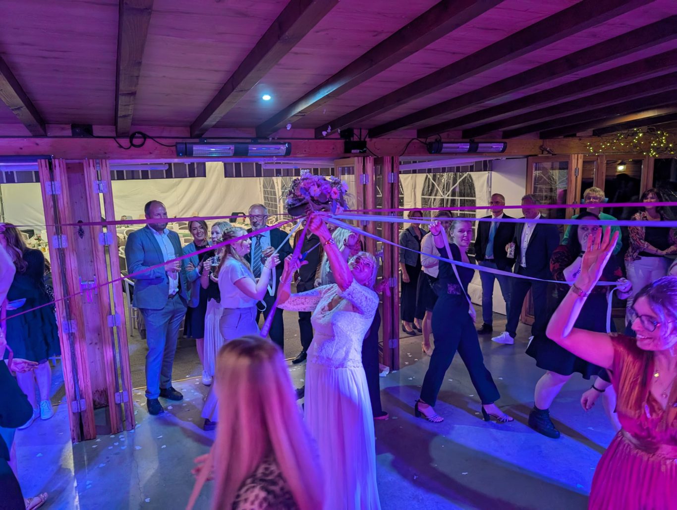 Brautstraußtanz in der schwarzenauer Mühle Party mit tanzenden Gästen unter bunten Lichtern, eine Frau fängt einen Blumenstrauß.